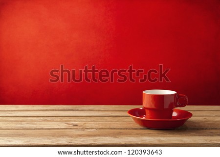 Red coffee cup on wooden table over red grunge background