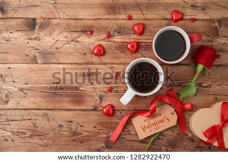 Valentine\'s day concept with coffee cups, heart shape chocolate, rose flower and gift box on wooden background. Top view from above. Flat lay