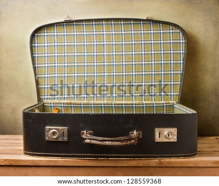 Empty vintage open suitcase on wooden table over grunge background