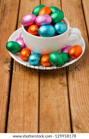 Easter chocolate eggs in coffee cup over wooden background. Easter table decoration