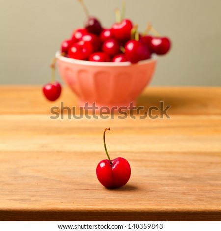 Single cherry over full bowl of cherries