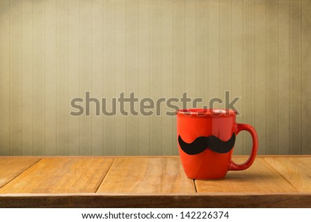 Red Cup With Paper Mustache On Wooden Table Over Retro Wallpaper