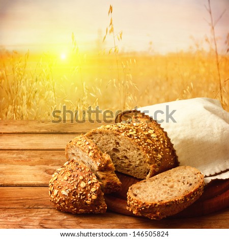 Fresh bread on wooden table over wheat field with sunset or sunrise