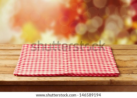Empty wooden table with red checked tablecloth over autumn leaves bokeh background. Ready for product montage