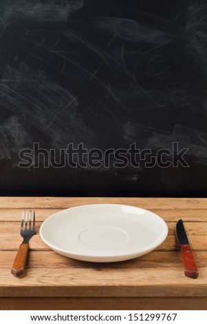 Empty plate with knife and fork on wooden table over chalkboard background