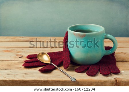 Cup of tea with lipstick stain and wool gloves on wooden table