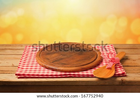 Round board on tablecloth on wooden table over bokeh background. Ready for product montage display