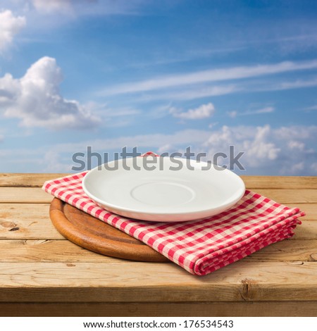 Plate and tablecloth on wooden table over blue sky