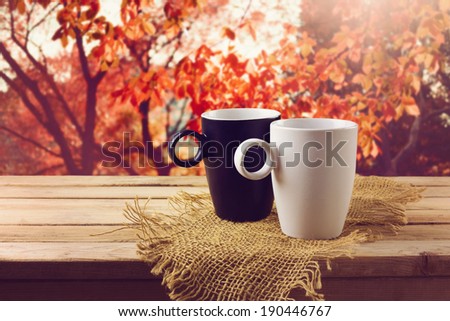 White and black cup with beverage on wooden table over beautiful nature background