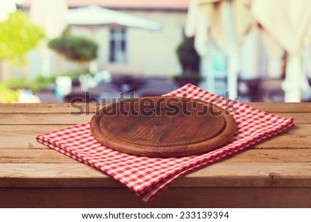 Wooden round board on tablecloth over restaurant background