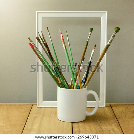 Painter brushes in white cup on wooden table. Cup for logo display mock up