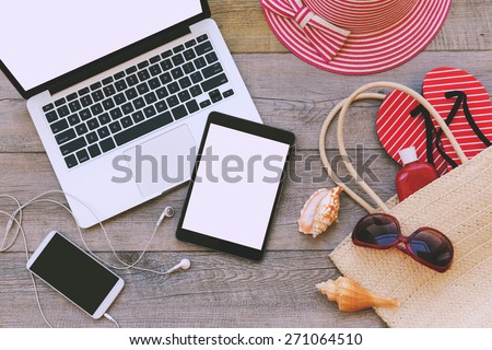Laptop, digital tablet and smart phone with beach items over wooden background. View from above