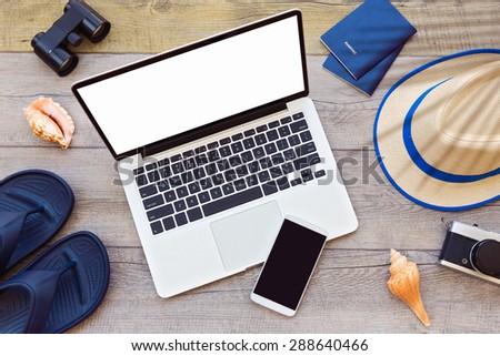 Laptop computer and smart phone with male summer holiday accessories on wooden board