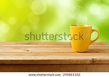 Yellow cup on wooden table over green bokeh background
