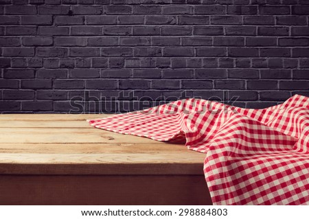 Wooden table background with red checked tablecloth over black brick wall