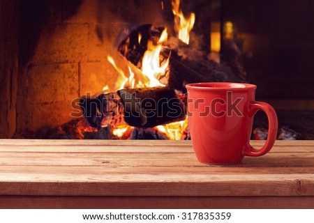 Red cup over fireplace on wooden table. Winter and Christmas holiday concept