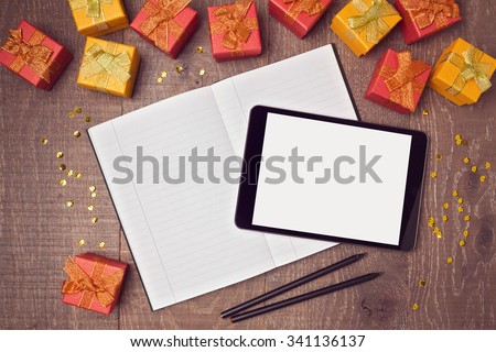 Digital tablet mock up template with gift boxes and notebook on wooden desk. View from above