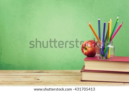 Back to school background with books, color pencils and apple over green wallpaper