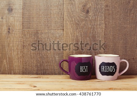 Coffee cups on wooden table with chalkboard sign and best friends text. Friendship day celebration background