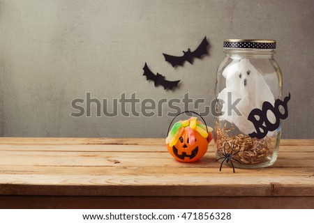 Halloween holiday decoration with ghost in jar and candy on wooden table