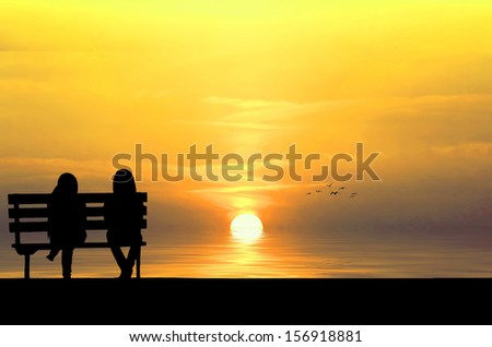 Silhouette of two friends sitting on wood bench near beach staring at flying bird