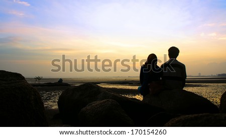 Silhouette of couple sitting on the rock looking at the sun goes down