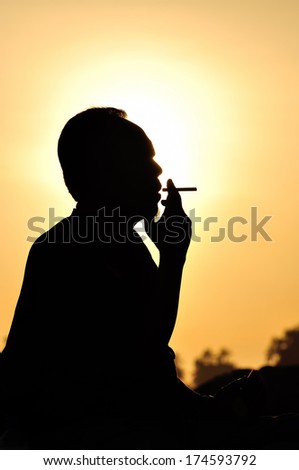 A man smoking cigarette over golden sunset
