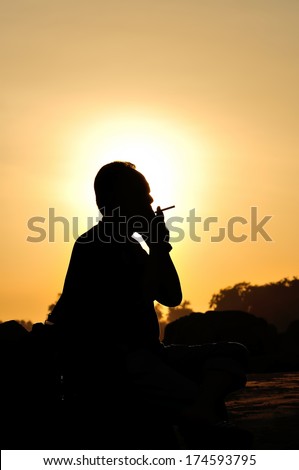 A man smoking cigarette over golden sunset