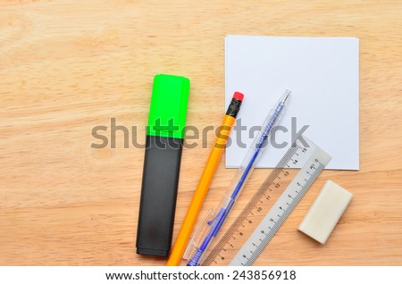 Blank post-it with pen, pencil, ruler, highlight market and eraser on office wooden table. Above view
