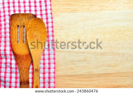 Wood background with copyspace bordered by a red and white country cloth with wooden kitchen utensils lying on top of it
