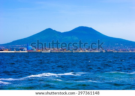 Blue seascape with mountains, and distant city in the back.
