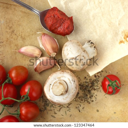 Organic cherry tomatoes, mushrooms, garlic and herbs on an old rustic stone chopping board. Pizza ingredients.