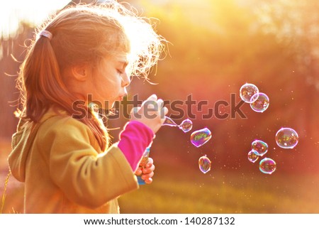 Five Years Old Caucasian Child Girl Blowing Soap Bubbles Outdoor At Sunset - Happy Carefree Childhood