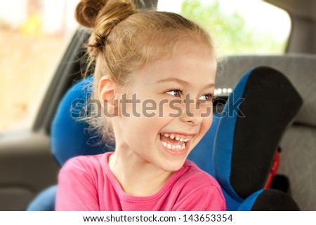 Portrait of happy five years old blond caucasian child girl laughing while traveling in a car seat