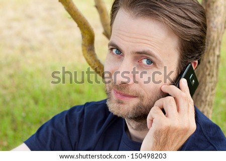 Close up portrait of happy smiling forty years old caucasian man talking on a mobile phone outdoor in a park