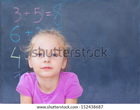 Young blond five years old caucasian girl in front of blackboard at school - mathematics lesson