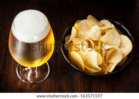 Beer glass and potato chips in a black bowl on dark wood background - snack bar or pub menu