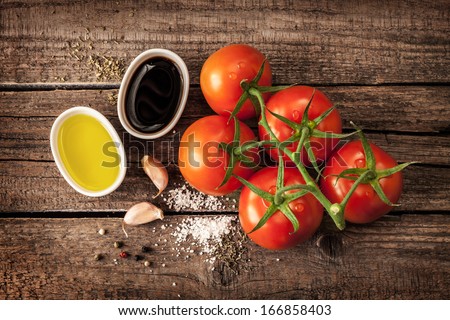 Vinaigrette or french dressing recipe ingredients and tomato branch on vintage wood background. Olive oil, balsamic vinegar, garlic, salt and pepper from above.