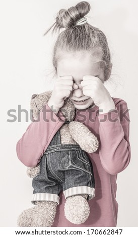 Small sad caucasian blond child girl crying while hugging teddy bear on a white background. Unhappy childhood concept.