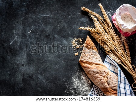 Rustic bread roll or french baguette, wheat and flour on black chalkboard. Rural kitchen or bakery - background with free text space.