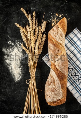 Rustic bread roll or french baguette, wheat and flour on black chalkboard. Rural kitchen or bakery.