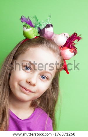 Portrait of happy smiling five years old blond caucasian child girl with colorful birds on head - pastel green background. Careless childhood and spring concept.