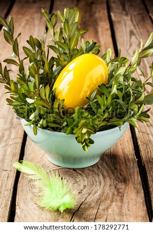 Easter decoration - yellow glossy egg and buxus in a blue bowl on an old vintage planked wood table. Rustic still life.