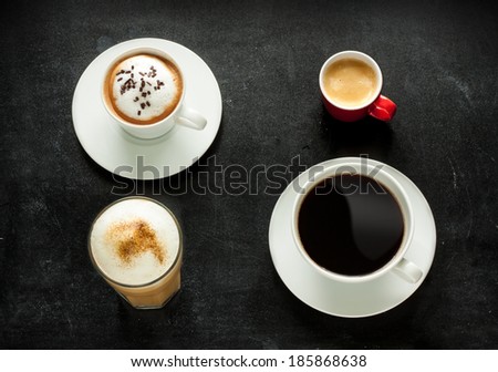Different kinds of coffee on black chalkboard background. Cappuccino, espresso, americana and latte from above - cafe menu.