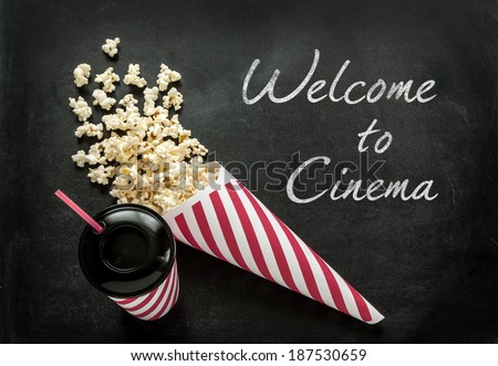 Welcome to cinema poster. Snacks - cornet popcorn and drink in paper cup with a straw on black chalkboard background.