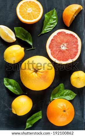 Citrus fruits (lemon, grapefruit and orange) with fresh wet leaves on black chalkboard background - still life from above