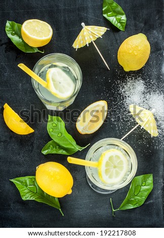 Lemonade with lemons and fresh wet leaves on black chalkboard background - still life from above