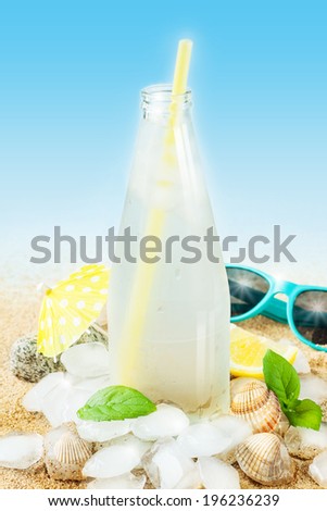 Cold water in a bottle with ice cubes on sand background - beach bar summer holiday cold beverages menu. Layout with free text space.