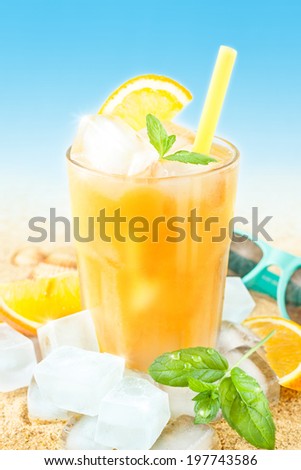 Cold orange juice in a tall glass with mint leaves and ice cubes on sand background - beach bar summer holiday beverages menu.