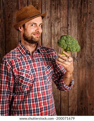 Happy smiling caucasian forty years old farmer or gardener in a hat holding broccoli in hand on rustic vintage planked wood background - agriculture. Food production - vegetables.